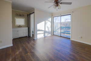 Empty room featuring a barn door, ceiling fan, dark hardwood / wood-style floors, crown molding, and sink