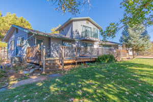 Rear view of house featuring a lawn, a balcony, and a wooden deck