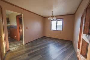 Empty room featuring dark hardwood / wood-style flooring, ornamental molding, a textured ceiling, and a notable chandelier