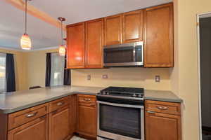 Kitchen with kitchen peninsula, appliances with stainless steel finishes, crown molding, and pendant lighting