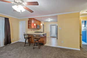 Kitchen featuring ceiling fan, a kitchen breakfast bar, kitchen peninsula, and light carpet