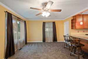 Kitchen featuring a textured ceiling, ceiling fan, dark carpet, and crown molding