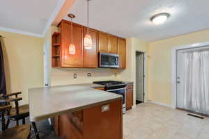 Kitchen featuring kitchen peninsula, appliances with stainless steel finishes, ornamental molding, a textured ceiling, and pendant lighting