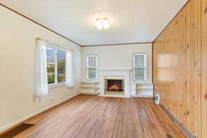 Unfurnished living room featuring a fireplace, wood walls, light hardwood / wood-style flooring, and ornamental molding