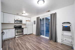 Kitchen with tasteful backsplash, stainless steel appliances, white cabinetry, and dark hardwood / wood-style floors