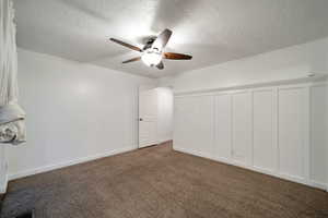 Additional living space featuring a textured ceiling, dark carpet, and ceiling fan