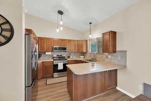 Kitchen with pendant lighting, sink, light hardwood / wood-style flooring, appliances with stainless steel finishes, and kitchen peninsula