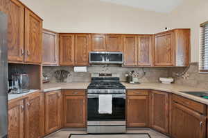 Kitchen featuring backsplash, stainless steel appliances, and vaulted ceiling