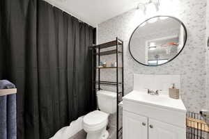 Bathroom with a shower with shower curtain, vanity, toilet, and a textured ceiling