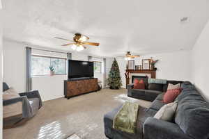 Carpeted living room featuring a tile fireplace, a textured ceiling, and ceiling fan