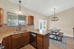 Kitchen with dishwasher, hanging light fixtures, kitchen peninsula, light hardwood / wood-style floors, and vaulted ceiling