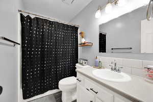 Bathroom featuring vanity, decorative backsplash, a shower with shower curtain, and toilet