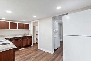 Kitchen with sink, dark hardwood / wood-style floors, a textured ceiling, dark brown cabinetry, and stacked washer / dryer