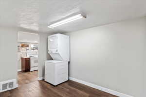 Laundry room with stacked washer and dryer, hardwood / wood-style floors, and a textured ceiling