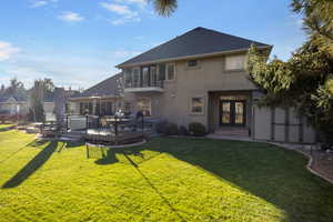 Rear view of house featuring a lawn, a balcony, french doors, and a deck