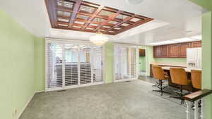 Kitchen with coffered ceiling, light colored carpet, pendant lighting, a chandelier, and white fridge with ice dispenser