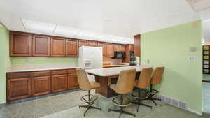 Kitchen with a breakfast bar, kitchen peninsula, white fridge with ice dispenser, and light colored carpet