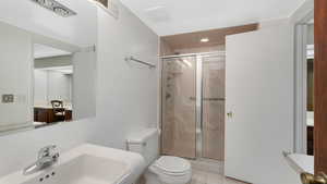 Bathroom with tile patterned flooring, toilet, a shower with shower door, and sink