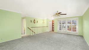 Carpeted empty room with ceiling fan with notable chandelier and crown molding