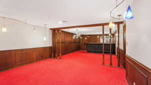 Basement with a notable chandelier, light carpet, and wooden walls