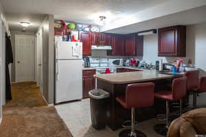 Kitchen featuring a kitchen breakfast bar, kitchen peninsula, a textured ceiling, and white appliances