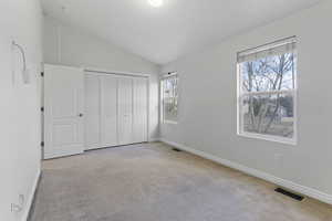 Unfurnished bedroom featuring multiple windows, light colored carpet, and vaulted ceiling