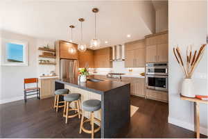 Kitchen featuring wall chimney exhaust hood, dark hardwood / wood-style floors, stainless steel appliances, and decorative light fixtures