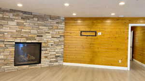 Unfurnished living room with light wood-type flooring, a stone fireplace, and wooden walls