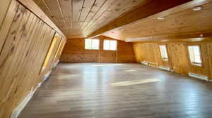 Bonus room featuring wood walls, wooden ceiling, a baseboard heating unit, lofted ceiling with beams, and wood-type flooring