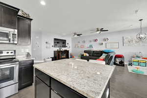 Kitchen with light hardwood / wood-style flooring, pendant lighting, a kitchen island, ceiling fan with notable chandelier, and appliances with stainless steel finishes