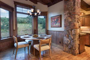 Dining area featuring wooden walls, light wood-type flooring, lofted ceiling with beams, and a notable chandelier