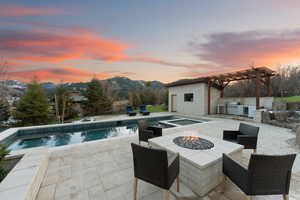 Pool at dusk with a fire pit, a mountain view, a pergola, area for grilling, and a patio