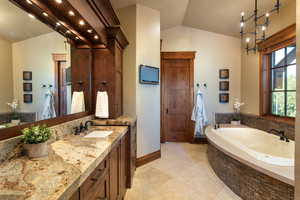 Bathroom featuring vanity, lofted ceiling, tile patterned floors, tiled tub, and a notable chandelier