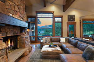 Living room with beam ceiling, a stone fireplace, ceiling fan, and hardwood / wood-style floors