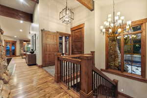 Hallway featuring beam ceiling, a chandelier, a towering ceiling, and light hardwood / wood-style floors