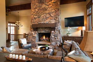 Living room featuring a notable chandelier, lofted ceiling with beams, wood-type flooring, and a fireplace