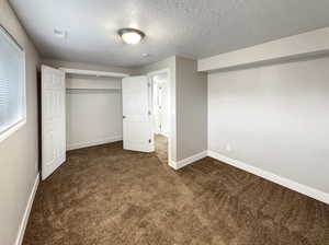 Unfurnished bedroom featuring a closet, a textured ceiling, and dark colored carpet