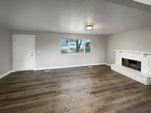 Unfurnished living room featuring a stone fireplace, dark wood-type flooring, and a textured ceiling