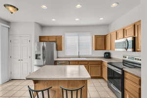 Kitchen with a breakfast bar, stainless steel appliances, sink, light tile patterned floors, and a kitchen island