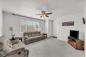 Carpeted living room with ceiling fan and a textured ceiling