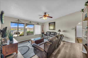 Living room featuring ceiling fan, vaulted ceiling, a textured ceiling, and light hardwood / wood-style flooring