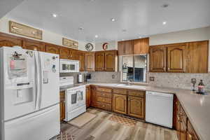 Kitchen with decorative backsplash, white appliances, sink, and light hardwood / wood-style flooring