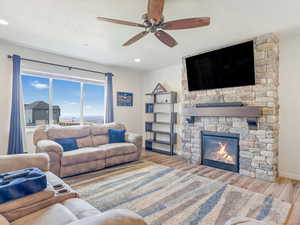 Living room with a textured ceiling, light hardwood / wood-style floors, a stone fireplace, and ceiling fan