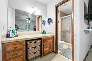 Bathroom featuring ceiling fan, vanity, an enclosed shower, and toilet