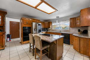 Kitchen with black appliances, sink, decorative light fixtures, a kitchen island, and a breakfast bar area