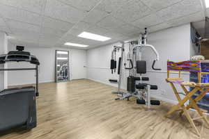 Exercise area featuring light wood-type flooring and a drop ceiling