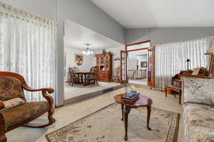 Carpeted living room featuring french doors, lofted ceiling, and a notable chandelier