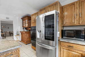 Kitchen featuring light stone countertops, appliances with stainless steel finishes, a textured ceiling, and light tile patterned floors