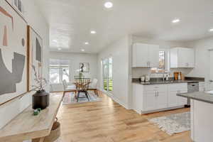 Kitchen with white cabinets, light hardwood / wood-style floors, stainless steel dishwasher, and sink