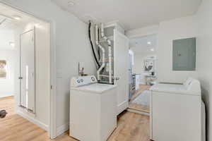 Washroom with electric panel, light hardwood / wood-style floors, and washing machine and clothes dryer